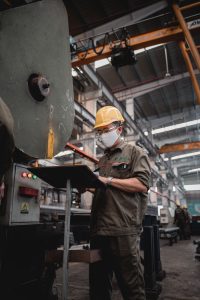 Factory worker in safety gear checking machinery