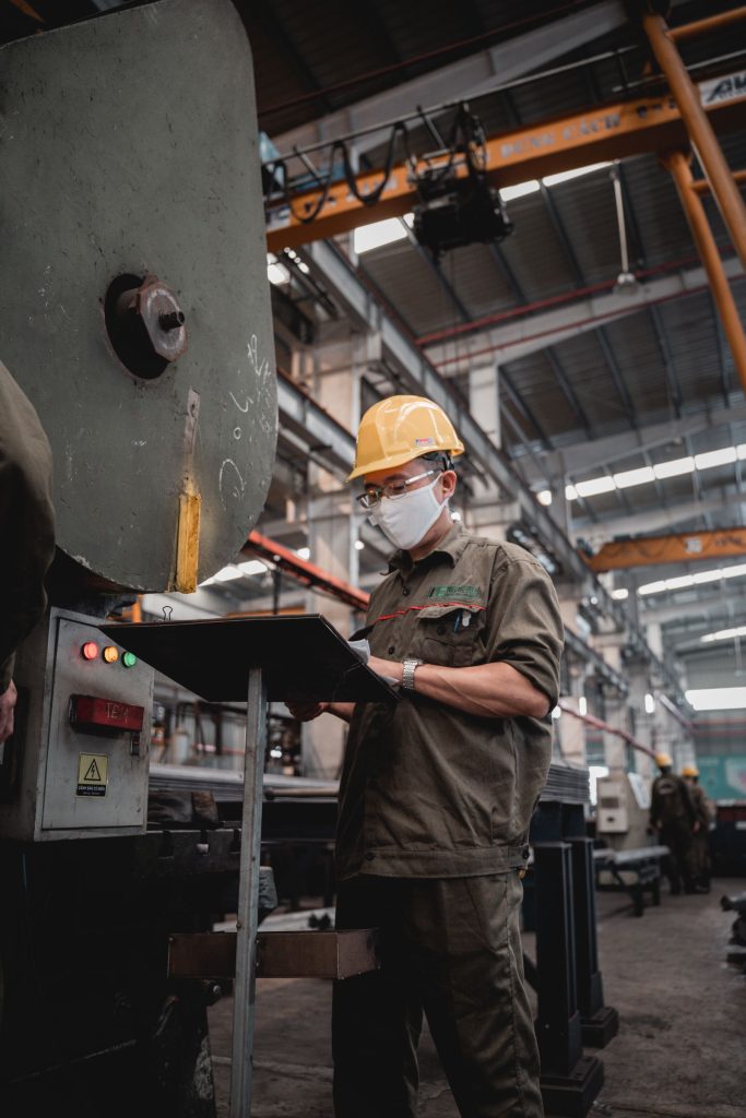 Factory worker in safety gear checking machinery