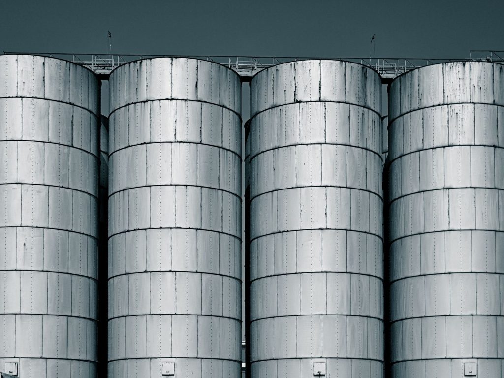 Four large steel storage silos against an overcast sky