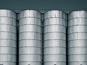 Four large steel storage silos against an overcast sky